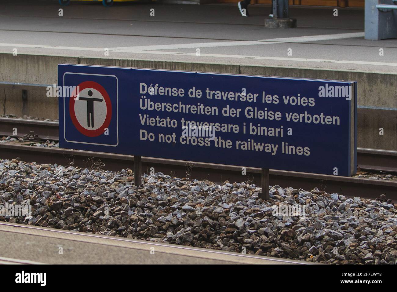 Schild zur Verhinderung der Überquerung der Eisenbahnschienen, weiße Schrift auf blauem Schild mit Schriften in verschiedenen europäischen Sprachen. Stockfoto