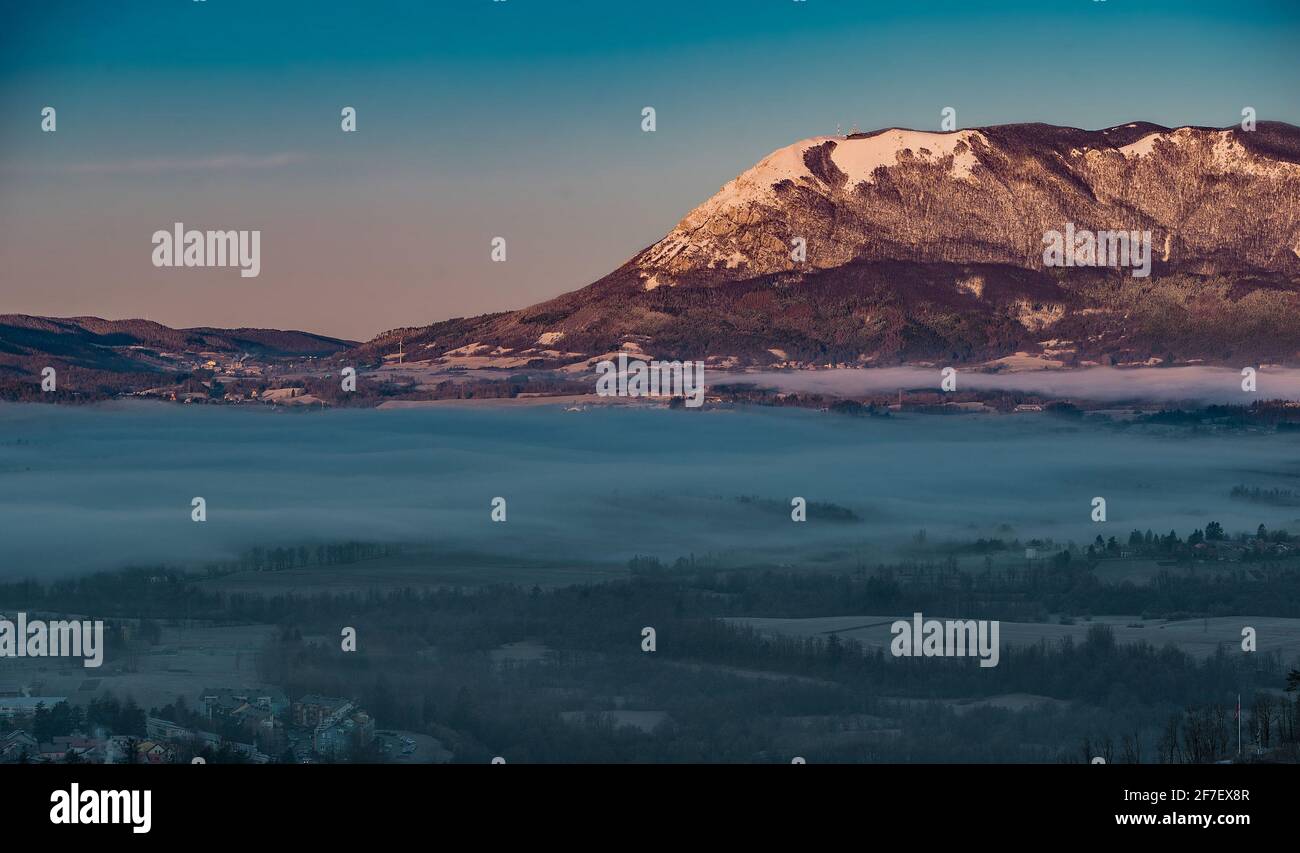 Der Berg Nanos, der in der Sonne über dem Tal von Postojna aufsteigt, ist immer noch von Nebel und Nebel bedeckt. Kontrast von gut und Böse am Morgen. Schöner Morgen Stockfoto