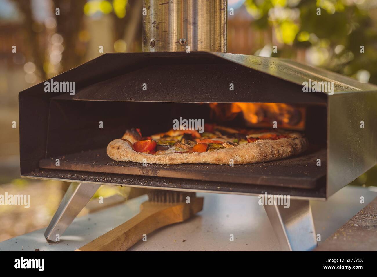 Hausgemachte Pizza wird in einem tragbaren Aluminium-Backofen für Pizza eingesetzt. Köstliche Pizza wird in einem Ofen gebacken, sichtbares Feuer auf der Rückseite des Furnás Stockfoto