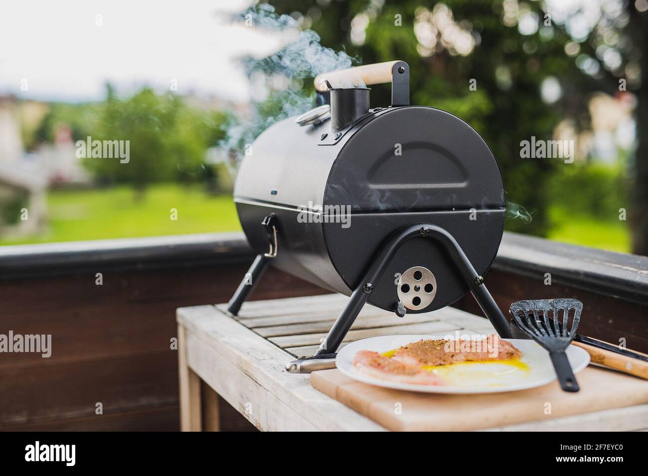 Rauch kommt aus einem Smokestack eines kleinen schwarzen Smoker Grill oder Grill auf grünem Hintergrund. Stockfoto