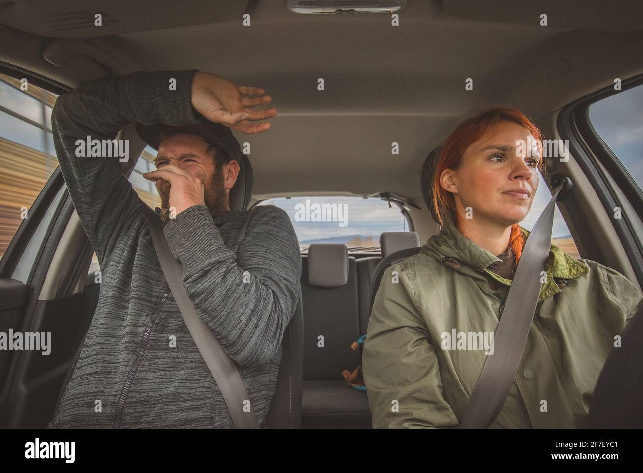 Eine Frau fährt ruhig ein Auto und ein Mann auf dem nächsten Sitz hat Angst wie die Hölle. Völlig verängstigte Beifahrerin wegen des rücksichtslosen fahrlässigen Fahrens durch eine Frau Stockfoto