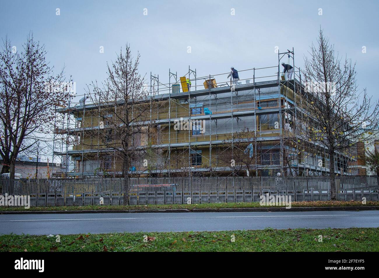 Metallgerüst an einem neuen Gebäude, das im Herbst bei kaltem Wetter gebaut wird. Auf dem Dach des Gebäudes sind Arbeiter zu sehen. Stockfoto