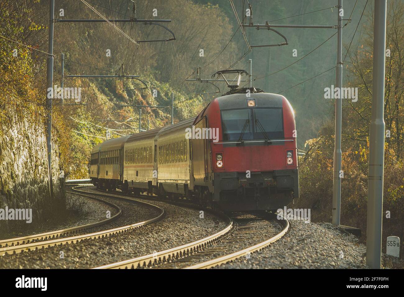 Personenzug auf einer Kurve mit einer modernen roten Lokomotive bei sonnigem Herbstwetter. Romantische Zugfahrt im frühen sonnigen Winter. Stockfoto