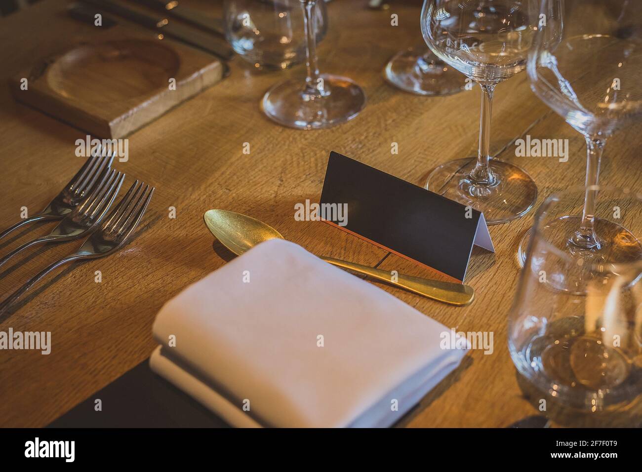 Leerer Namensschild auf einem Holztisch bei einem eleganten Dinner mit mehreren Gläsern, Gabeln und anderem Besteck. Wichtige Person Sitzplatz an einem di Stockfoto