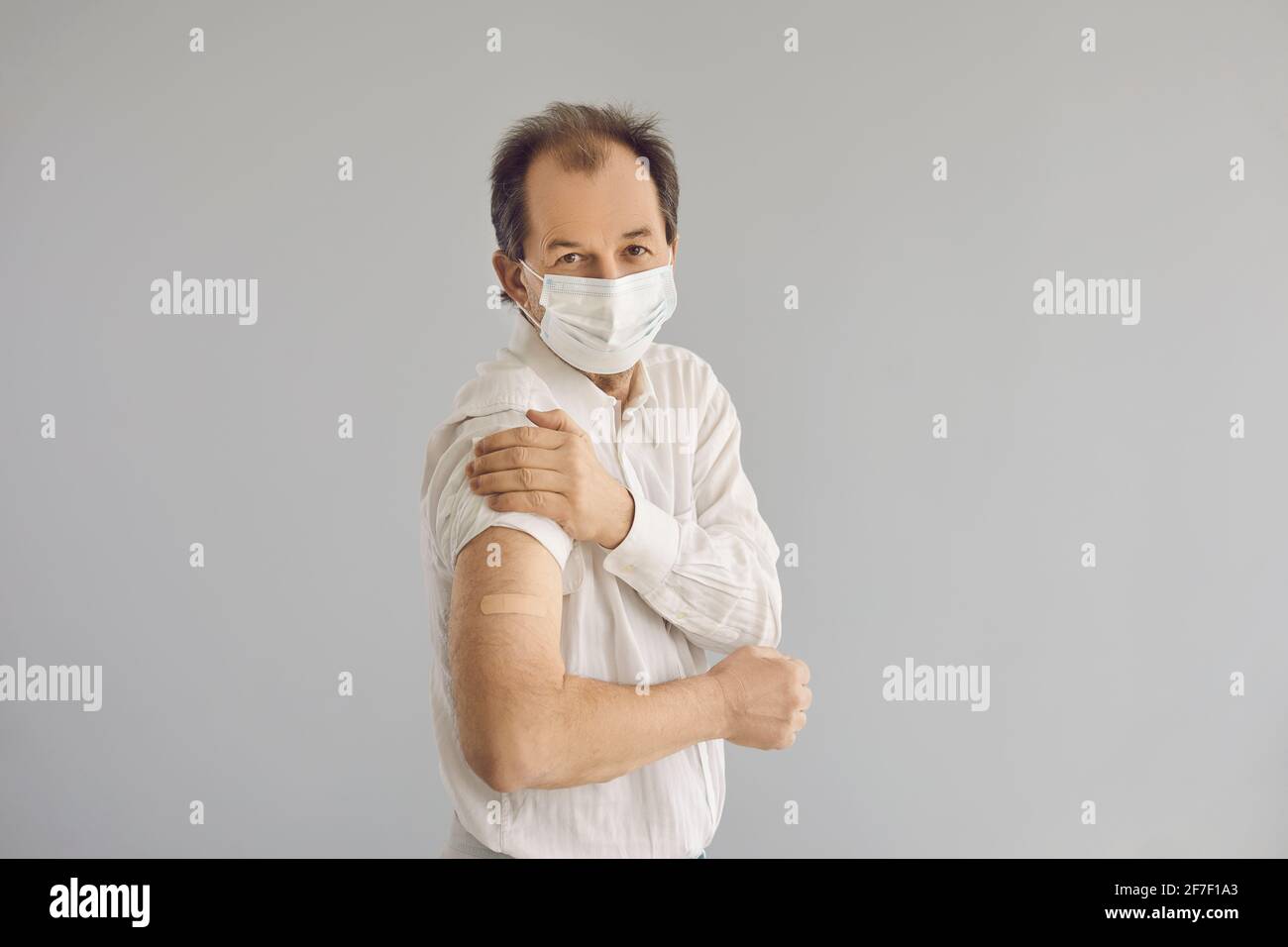 Porträt eines glücklichen älteren Mannes in Gesichtsmaske, der seinen zeigt Arm nach der Verabreichung des Impfstoffs Stockfoto