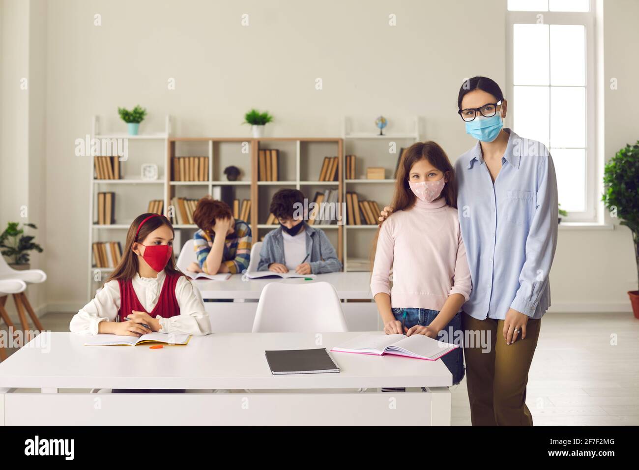 Lehrer umarmen Schüler stehen im Klassenzimmer mit anderen Jungen und Mädchen sitzen an Schreibtischen Stockfoto