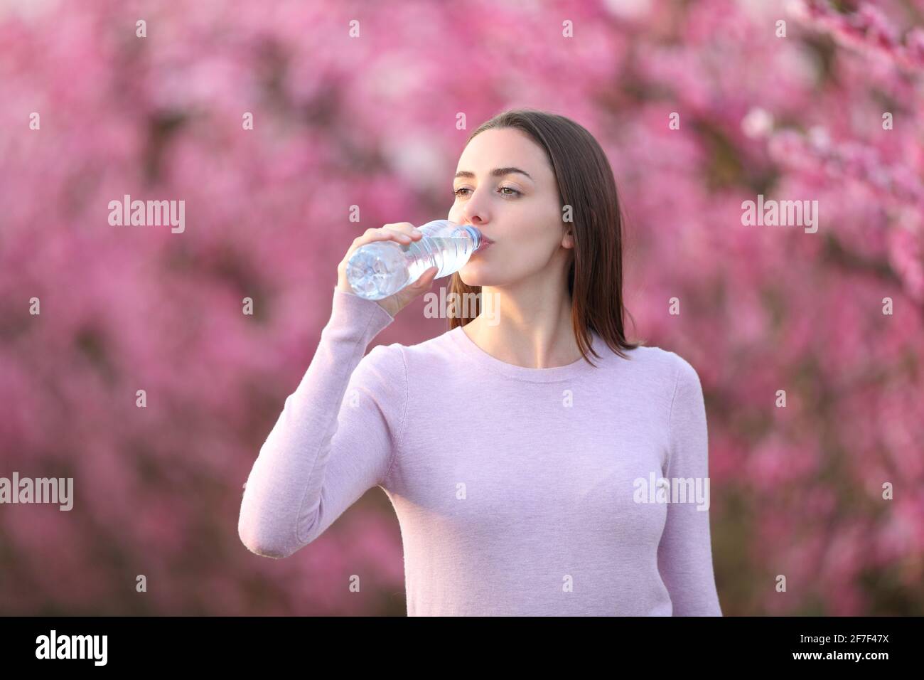 Entspannte Frau Hydrierung Trinkwasser aus der Flasche in einem rosa Blühtes Feld Stockfoto