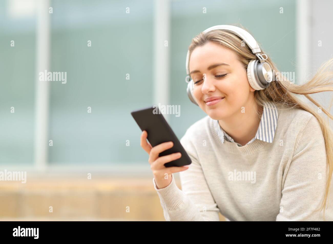 Zufriedener Teenager, der auf dem Smartphone im Sitzen Musik hört Die Straße Stockfoto
