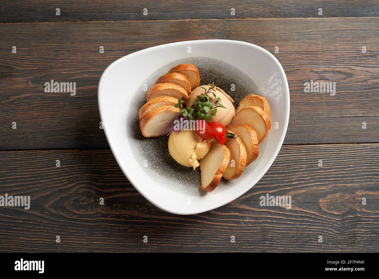 Draufsicht auf leberpastete-Kugeln in weißer Keramikplatte serviert mit frischen grünen Sprossen, Kirschtomaten und weißem Brot. Leckeres Gericht auf Holztisch im Café. Konzept der köstlichen Küche. Stockfoto