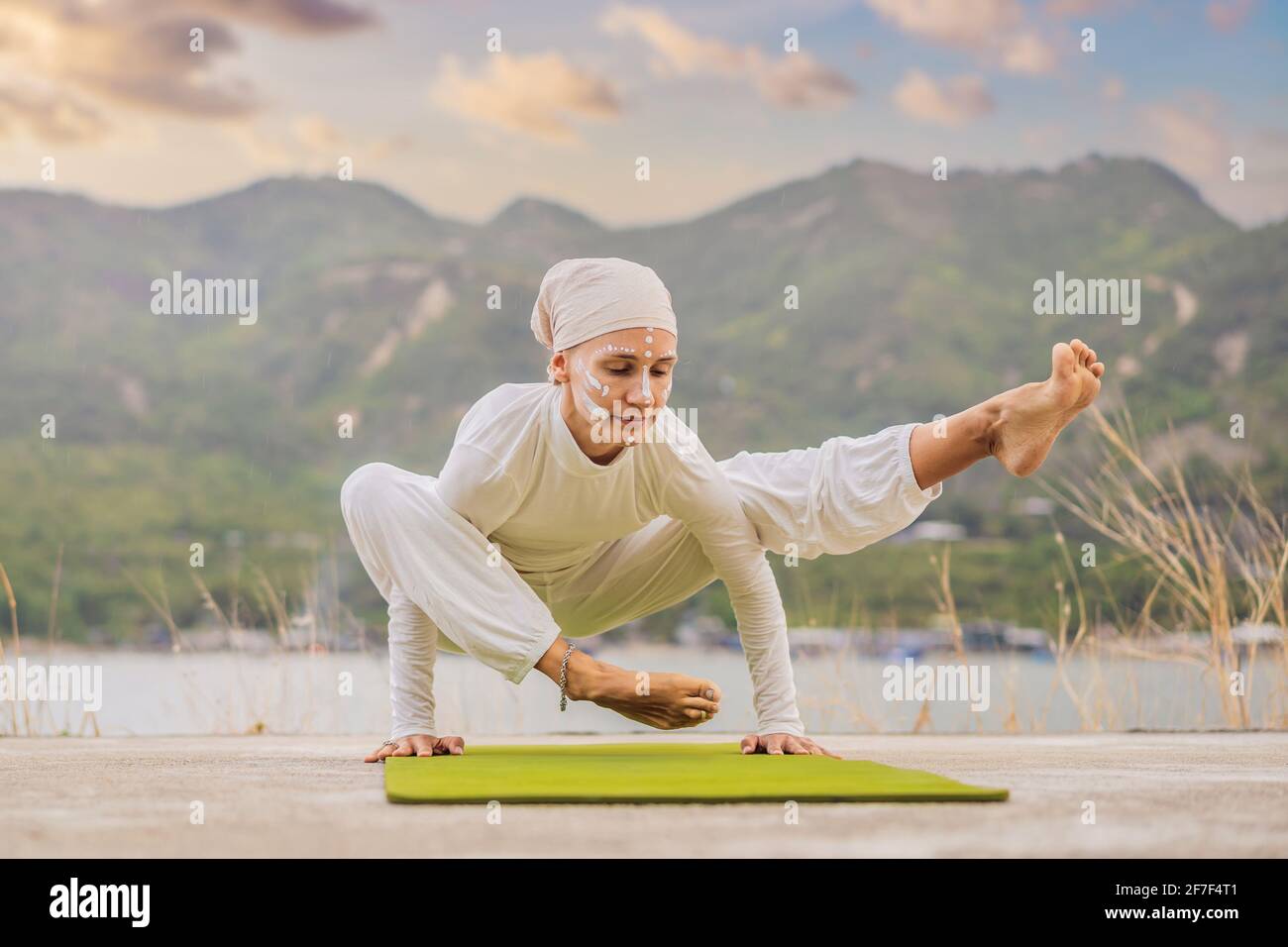 Kundalini Yoga Frau in weißen Kleidern und Turban praktiziert Yoga Kundalini auf dem Hintergrund des Meeres, der Berge und des Sonnenuntergangs. Fighting Face Painting Stockfoto