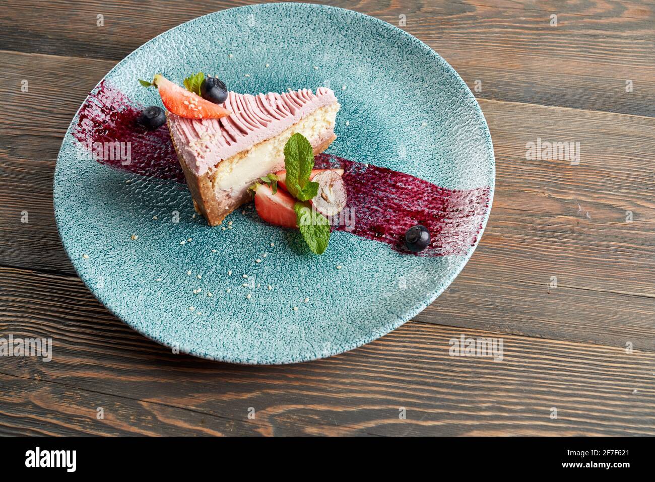 Von oben Blick auf den traditionellen Käsekuchen mit Heidelbeeren und Preiselbeeren auf dem Teller mit violettem Pinselstrich Dekoration serviert. Leckeres Essen auf einem Holztisch im Restaurant. Konzept von Dessert, Servieren. Stockfoto