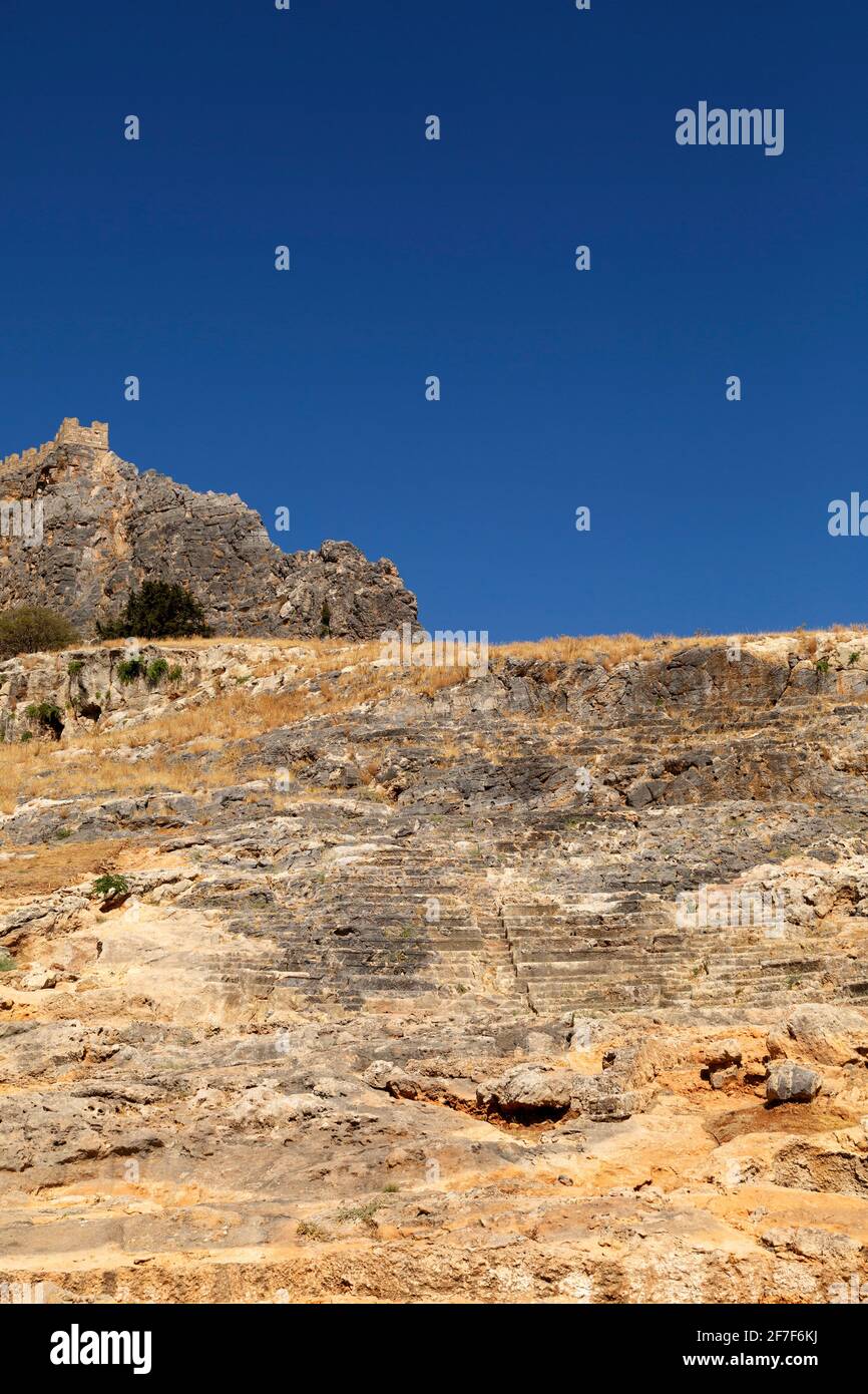Sitzplätze im antiken Theater am Fuße der Lindischen Akropolis in Lindos, auf Rhodos, Griechenland. Der Veranstaltungsort wurde als Ort der Unterhaltung genutzt. Stockfoto