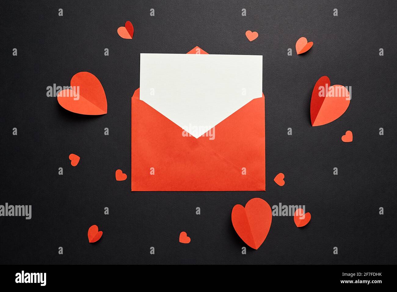 Grußkarten-Mockup mit Papierdekorationen auf schwarzem Hintergrund, flaches Lay. Valentinstag leere Grußkarte oder Einladung, Umschlag und rotes Papier er Stockfoto