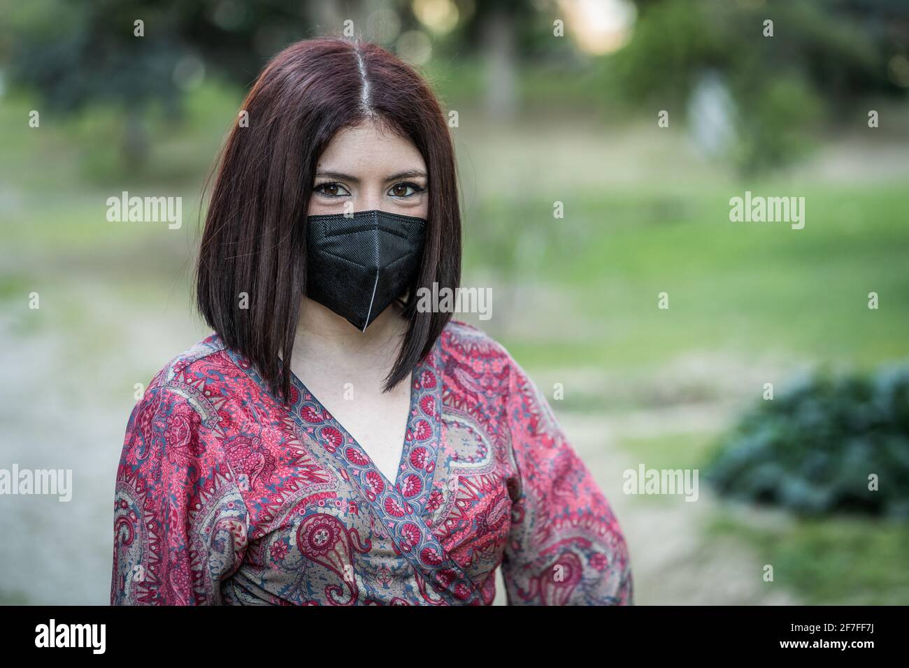 Junge Frau, die in einem Park in der Coronavirus-Maske wartet Stockfoto