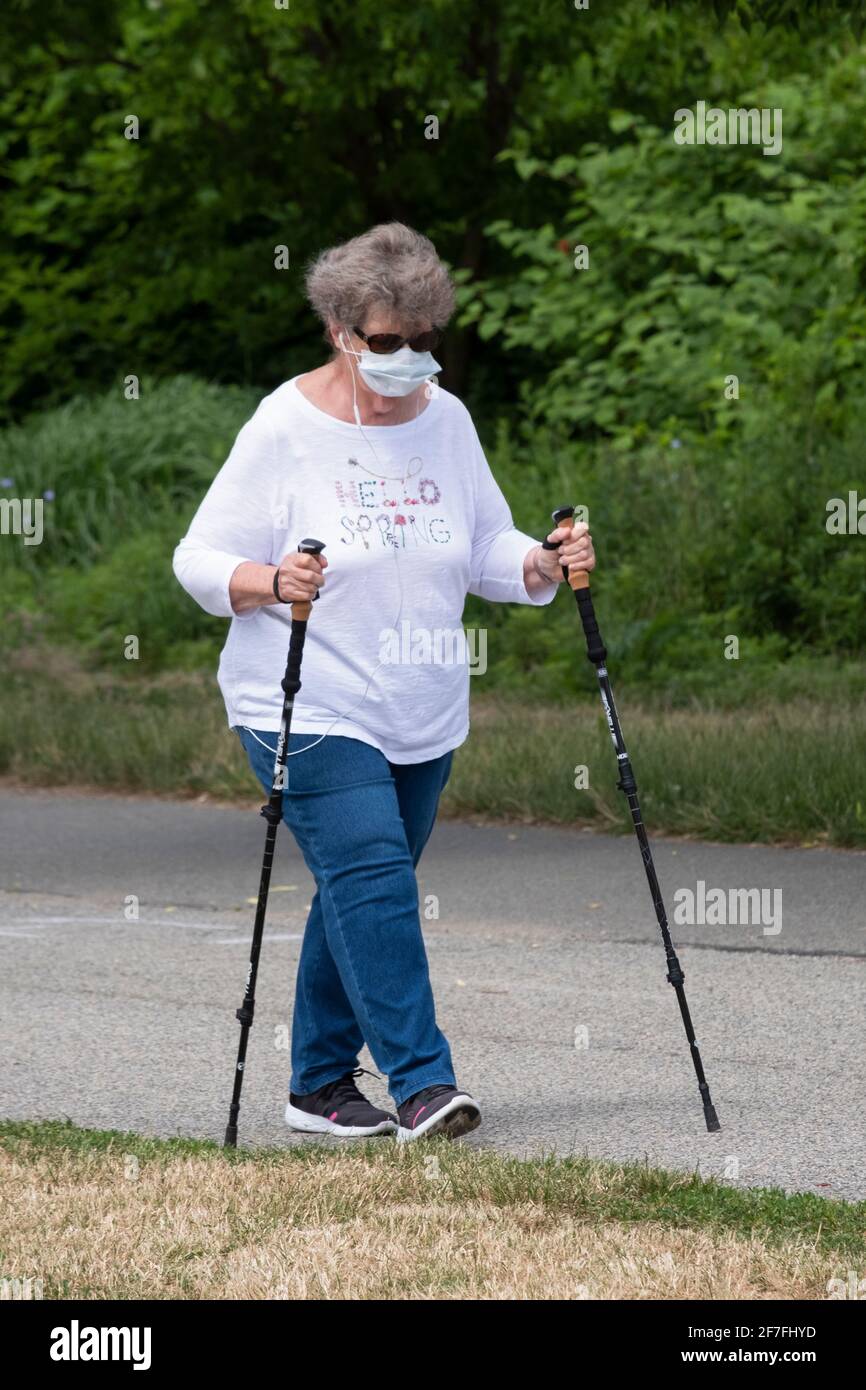 Eine ältere Frau, die im Little Bay Park in Whitestone, Queens, New York, mit Spazierstöcken spazieren geht und Musik hört. Stockfoto