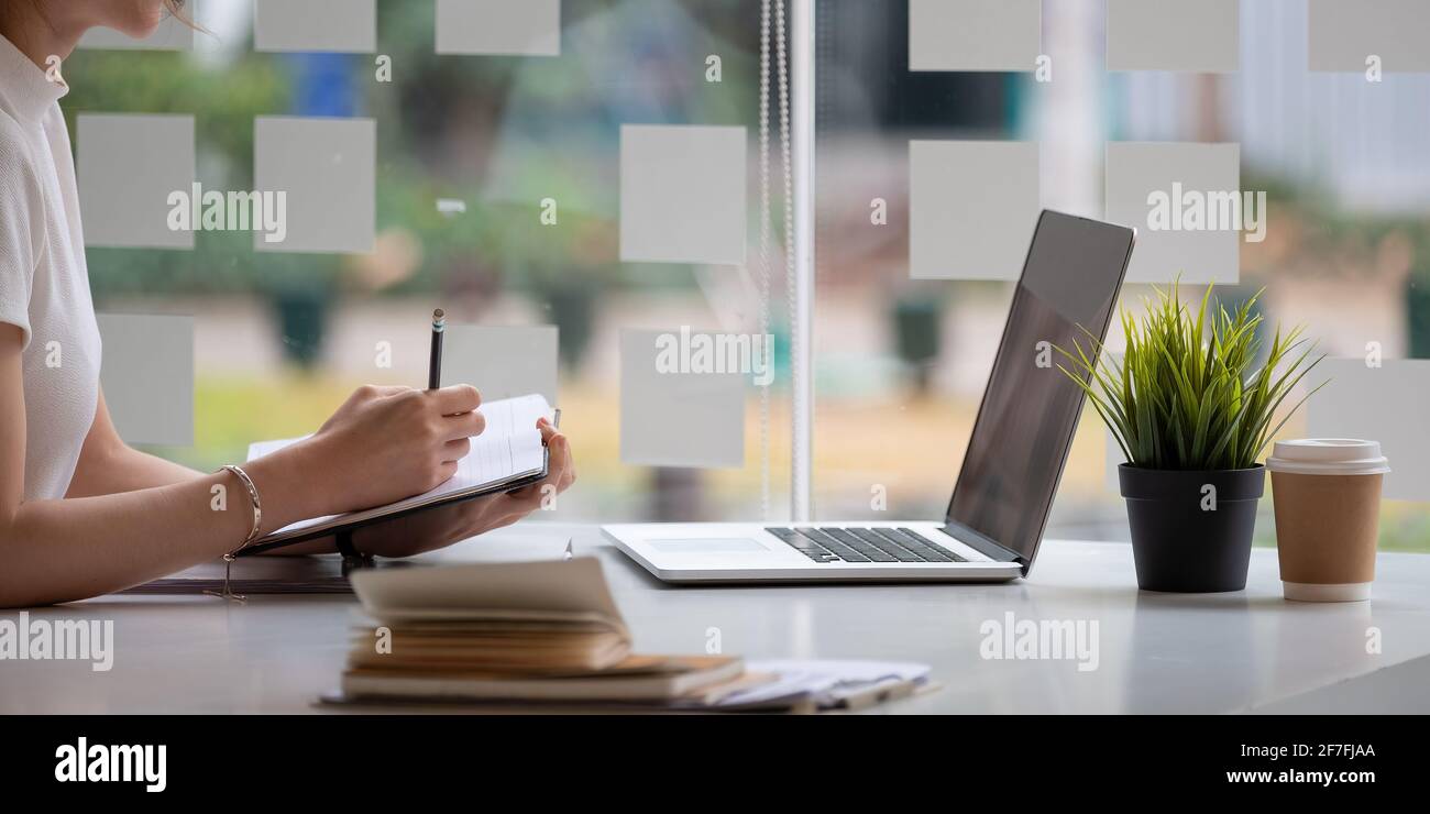 Nahaufnahme einer Geschäftsfrau, die auf Papier schreibt und verwendet Laptop auf die Suche nach Daten für die Arbeit oder Online-Lernen Stockfoto