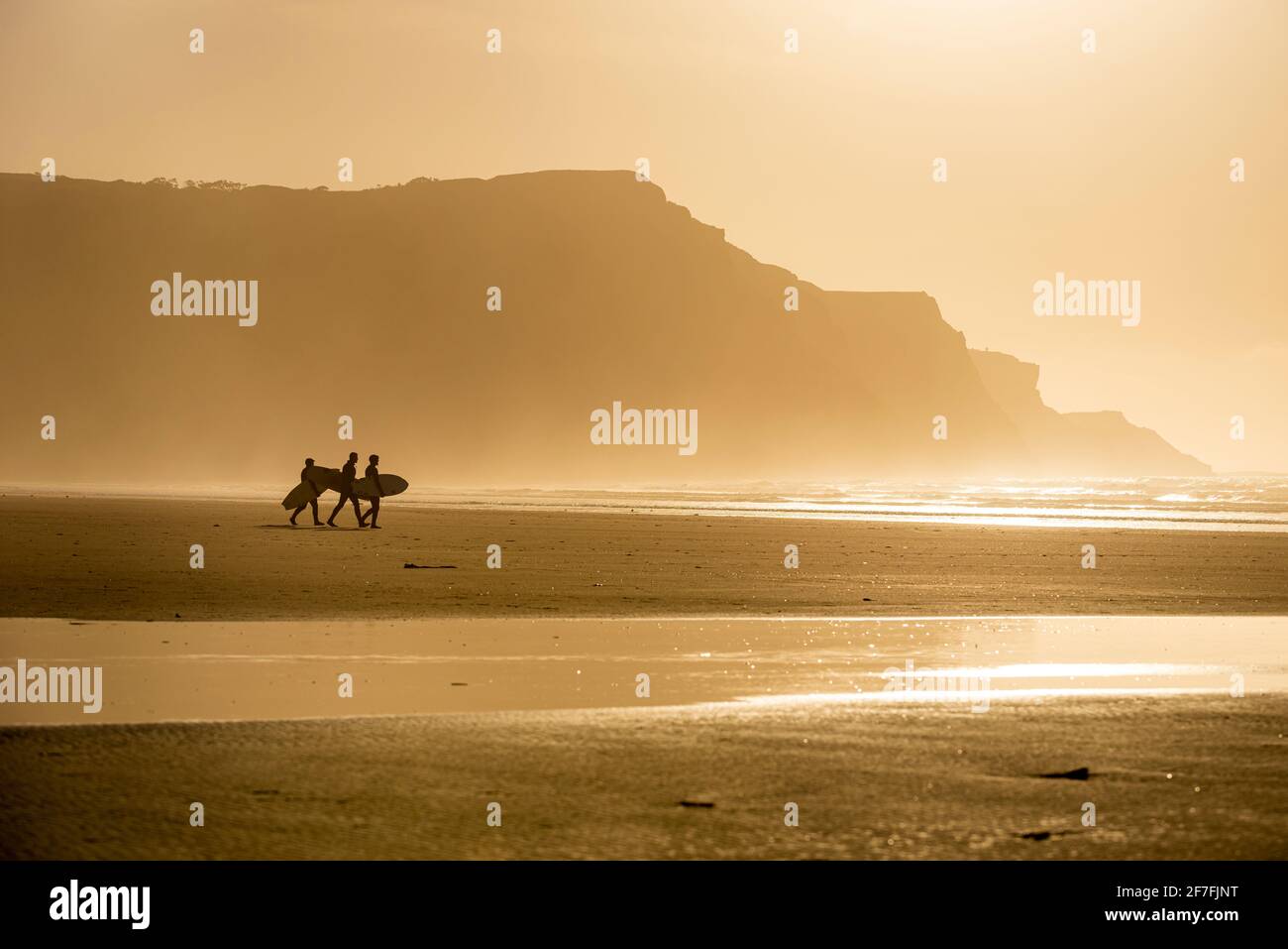 Menschen, die Surfbretter tragen, die im Abendlicht am Strand entlang laufen, Rhossili, Gower Peninsula, Swansea, Wales, Vereinigtes Königreich, Europa Stockfoto