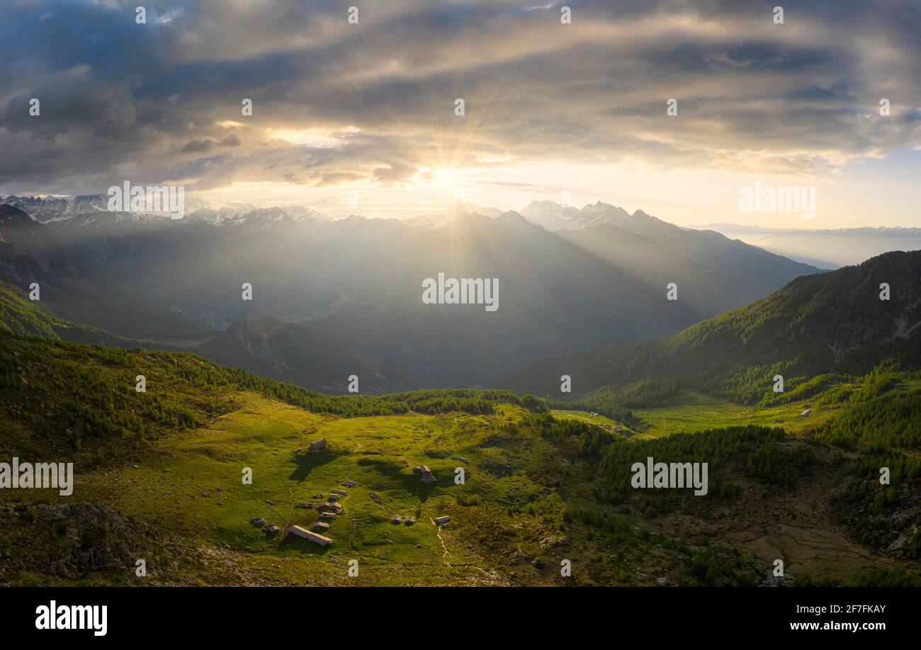 Sonnenfilter zwischen Wolken bei Sonnenaufgang mit beleuchteten Weiden, Valmalenco, Valtellina, Lombardei, Italien, Europa Stockfoto