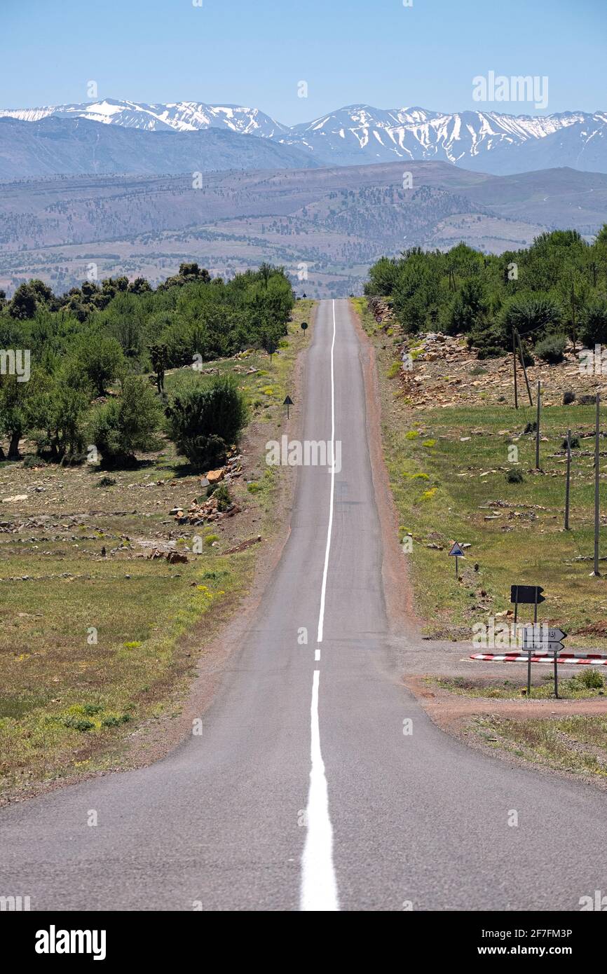Lange geteerte Straße mit dem verschneiten Atlasgebirge im Hintergrund, Marokko, Nordafrika, Afrika Stockfoto
