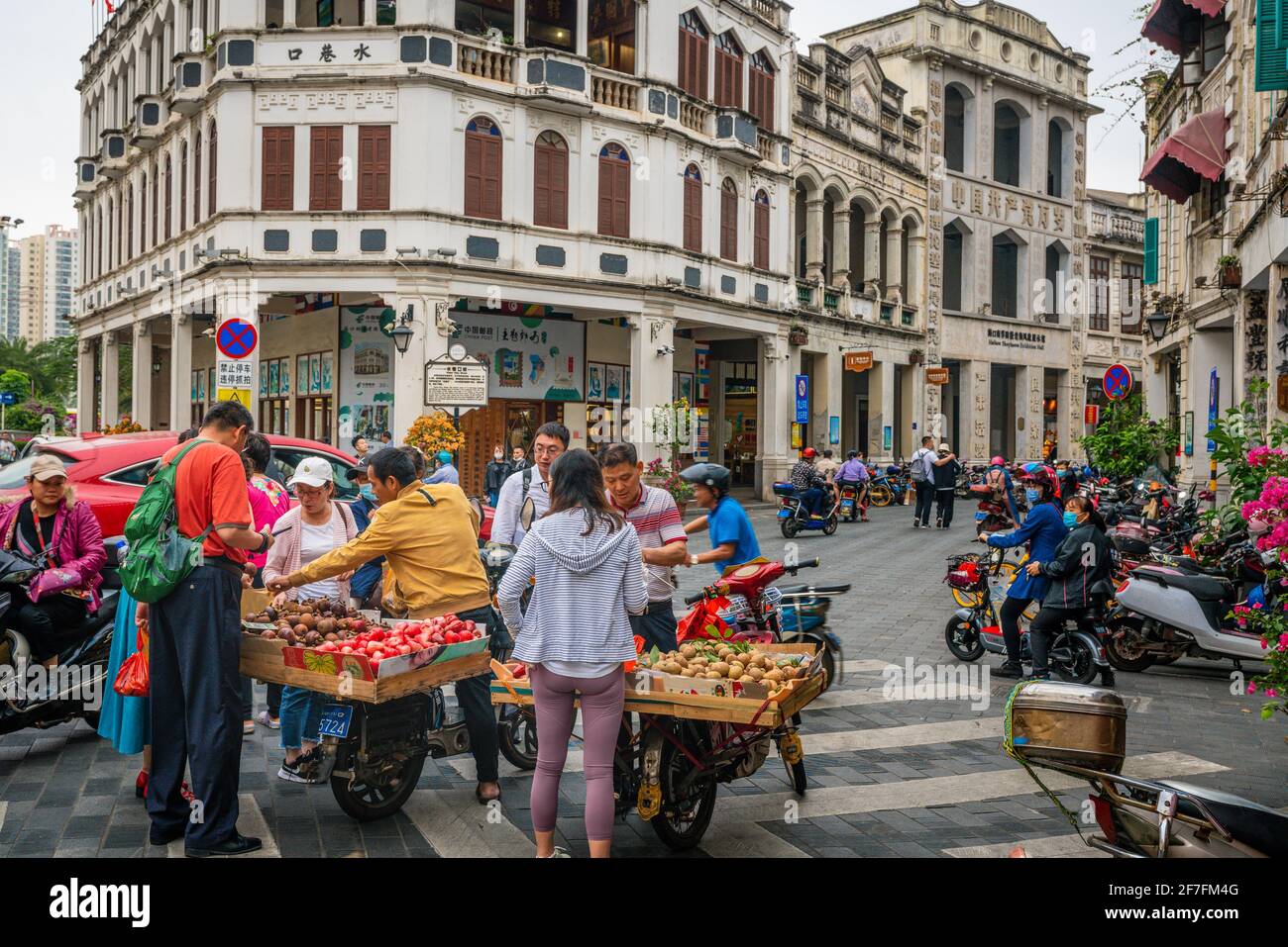 Haikou China , 21 March 2021 : Touristen kaufen Früchte an der Straße Lebensmittel-Stand in Wasser-Gasse Straße mit alten kolonialen Gebäuden und Menschen in Haikou alt Stockfoto