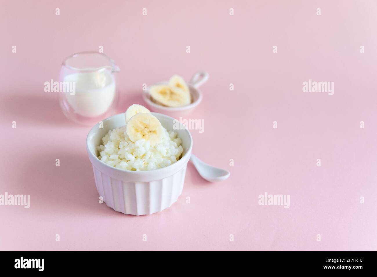 Reisbrei auf pflanzlicher Milch mit Bananenscheiben auf rosa minimalem Hintergrund. Diät gesundes Frühstück Stockfoto