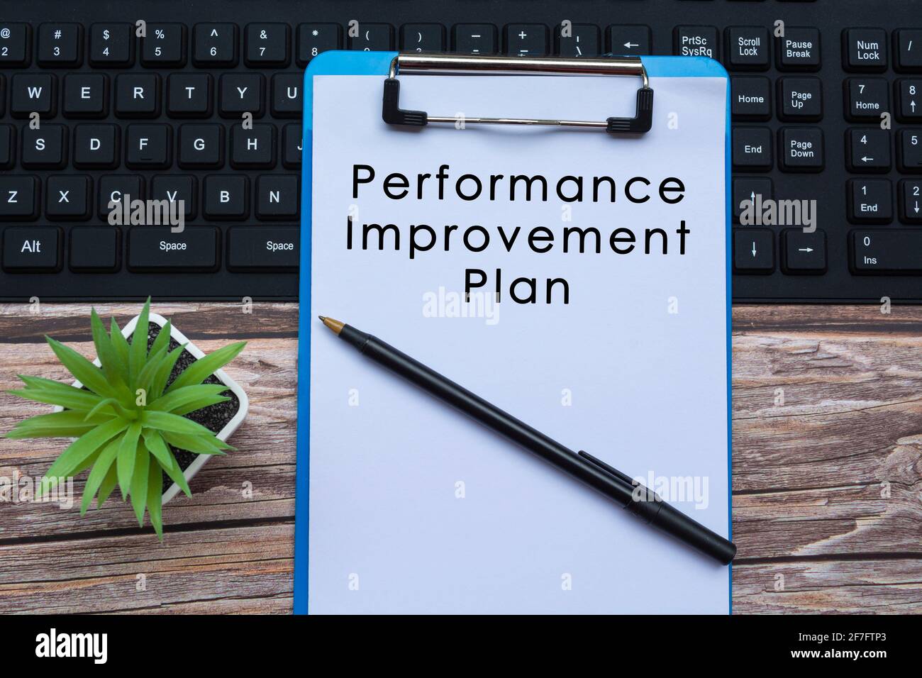 Text auf blauem Clipboard auf einer Tastatur mit Stift und Topfpflanze Stockfoto