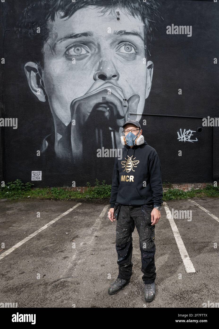 Der Straßenkünstler Akse steht vor seinem Wandbild von Joy Divisons Frontmann Ian Curtis. Stockfoto