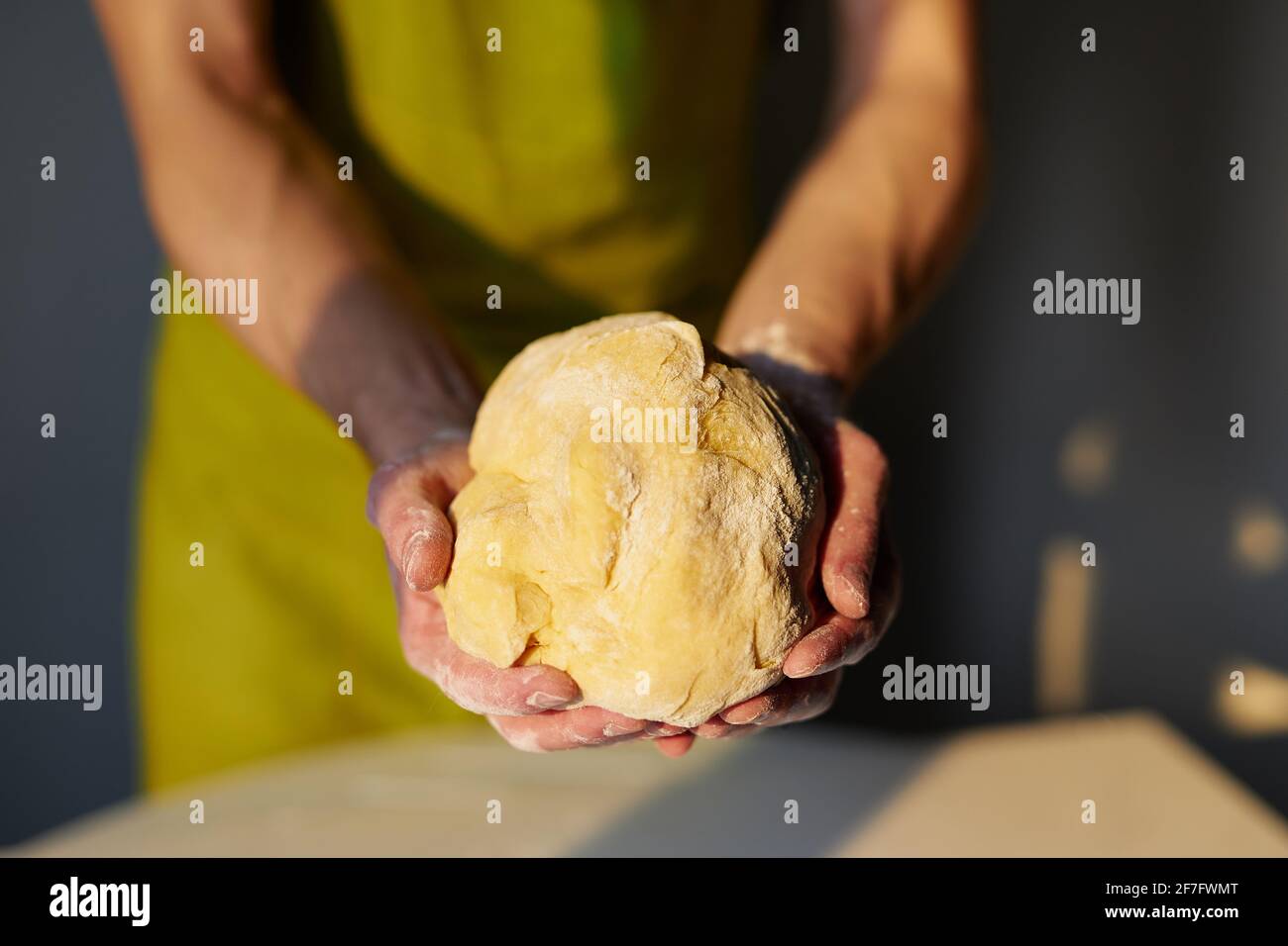 Hausgemachtes Gebäck backen, Ostergebäck vorbereiten oder leckeres Cookie-Konzept. Der Chefkoch in grüner Schürze hält in den Händen einen Teig, der für Brot, Pizza oder Gebäck hergestellt wurde. Hochwertige Fotos Stockfoto
