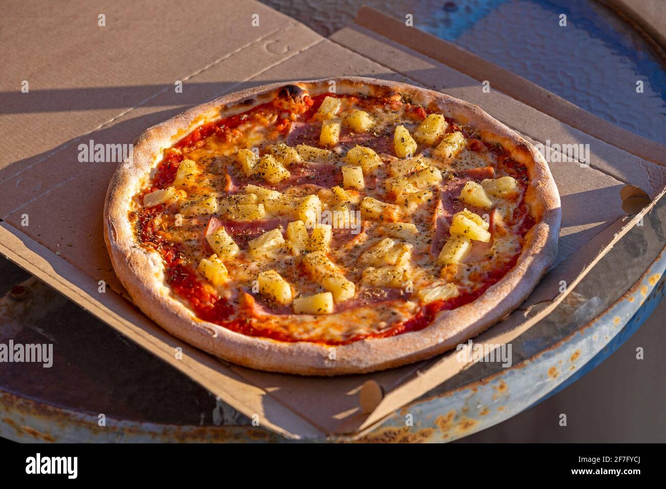 Pizza in einer Schachtel auf einem rostigen Tisch mit Tomatensauce, Käse, Schinken, Ananas, Orangano Stockfoto