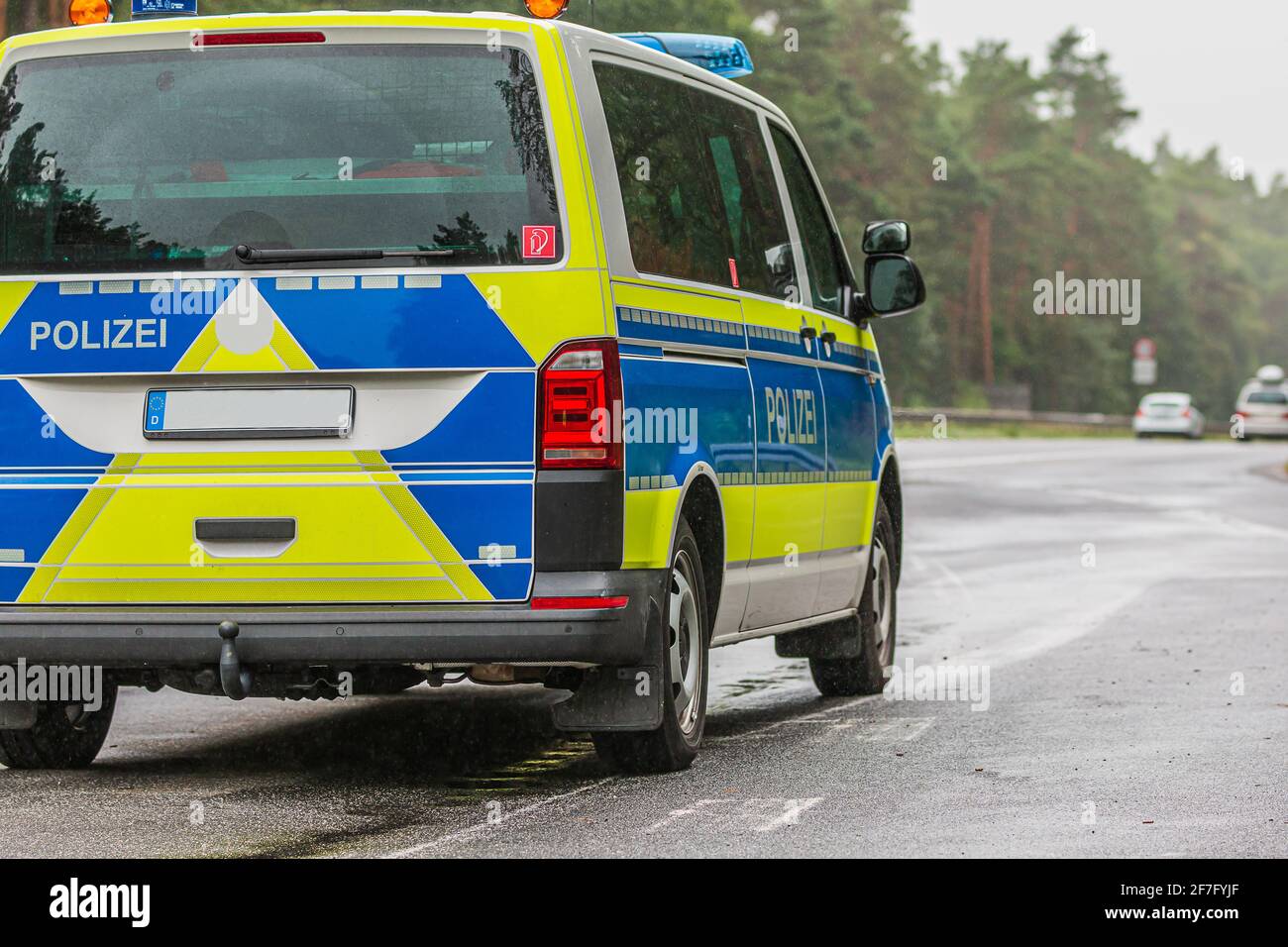 Polizeiauto auf der Autobahn im Land Brandenburg. Asphaltierte Straßenoberfläche bei Regenwetter. Abgewinkelte Ansicht des Fahrzeugs von hinten. Gelbblau Stockfoto