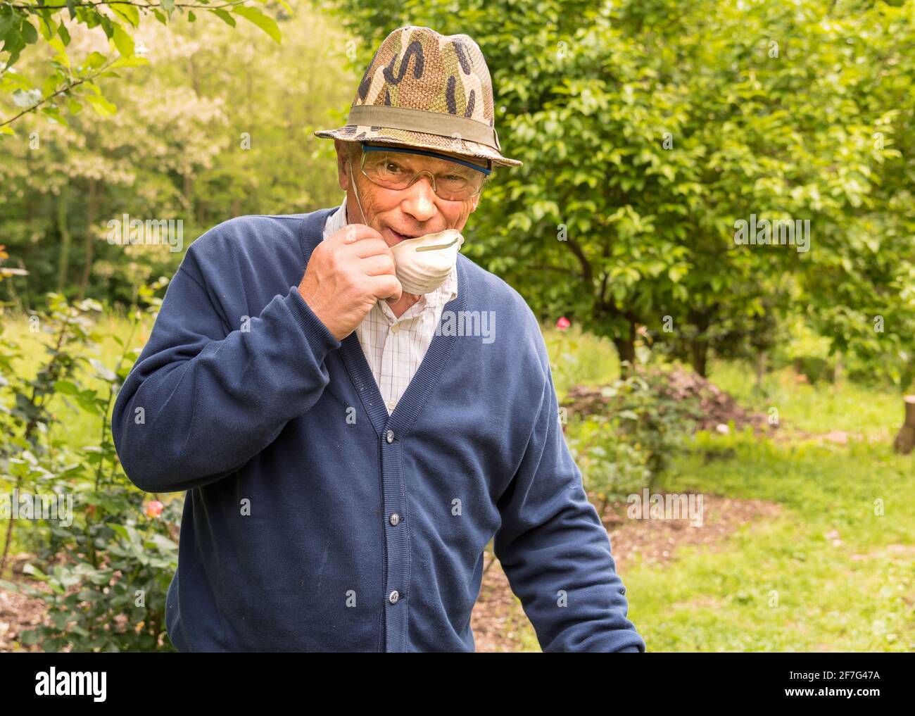 Älterer Mann mit Schutzbrille, Maske und Hut arbeitet im Garten. Stockfoto