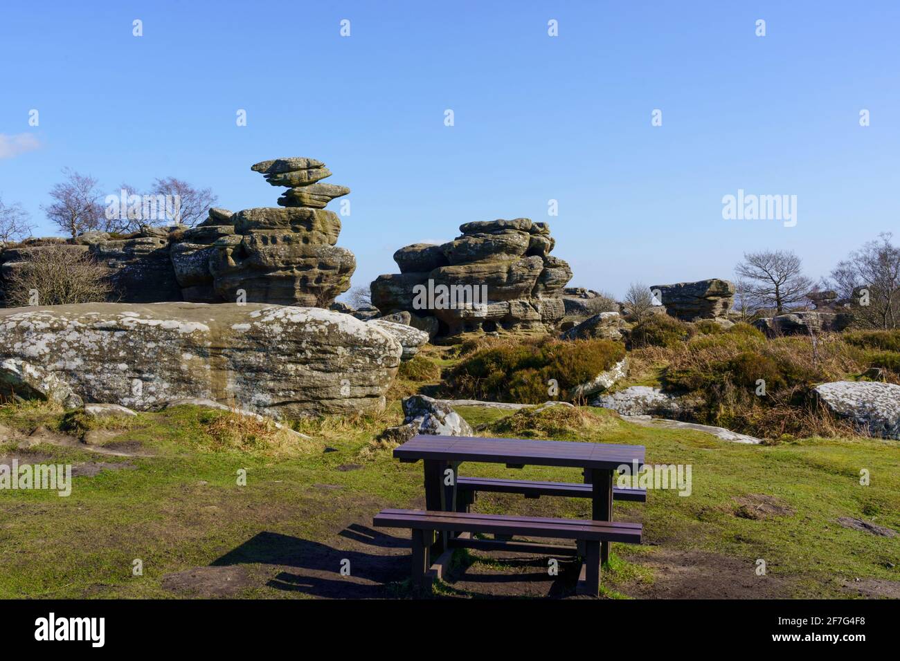 In Brimham Rocks, Nidderdale, gibt es einen langen Holzpicknicktisch mit atemberaubenden Felsformationen in der Ferne, Harrogate, North Yorkshire, Großbritannien. Stockfoto