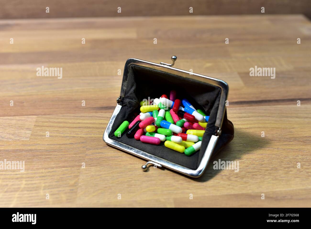 Pillen in Brieftasche auf Holzhintergrund. Bunte pharmazeutische Pillen, medizinische Tabletten und Kapseln im Geldbeutel. Pille sucht Konzept. Geld ausgeben Stockfoto