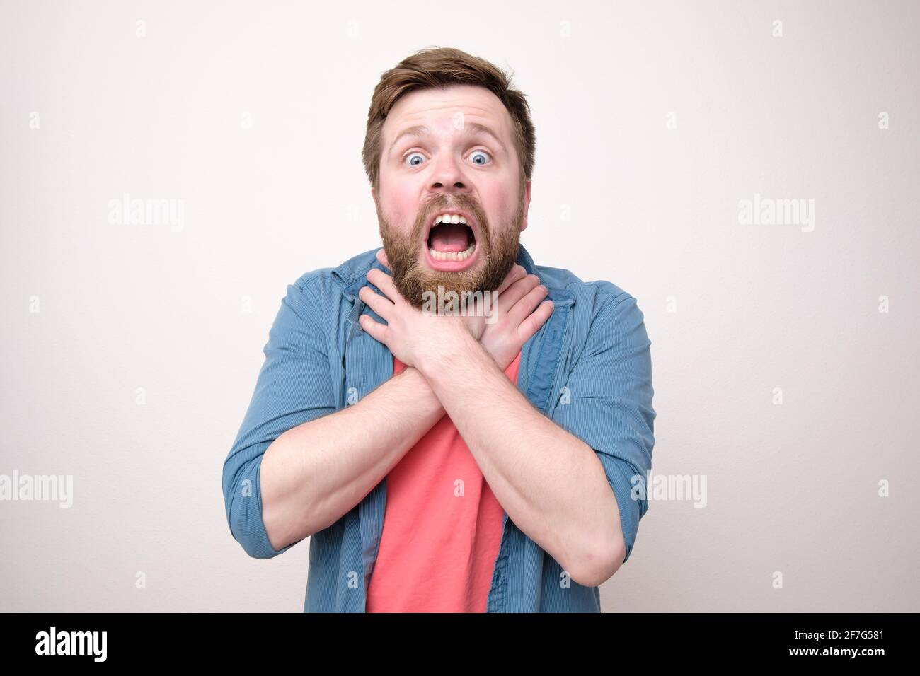 Verängstigter bärtiger Mann erstickt oder hat starke Halsschmerzen, hält die Hände bei geöffnetem Mund am Hals. Weißer Hintergrund. Stockfoto