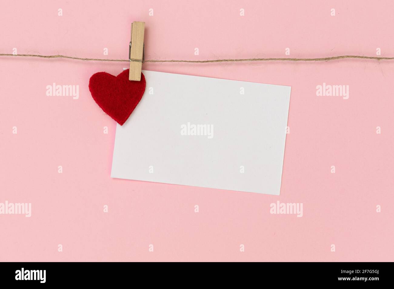 Weißes Stück Papier, mit Wäscheklammer am Seil befestigt, auf rosa Hintergrund. Alles gute zum Valentinstag. Stockfoto