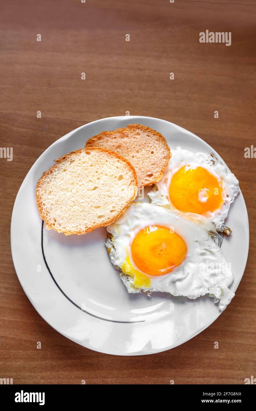 Ein Omelett aus Hühnereiern, frisch zubereitet, steht auf einem Teller und zwei Scheiben Weißbrot. Flaches Layout. Stockfoto