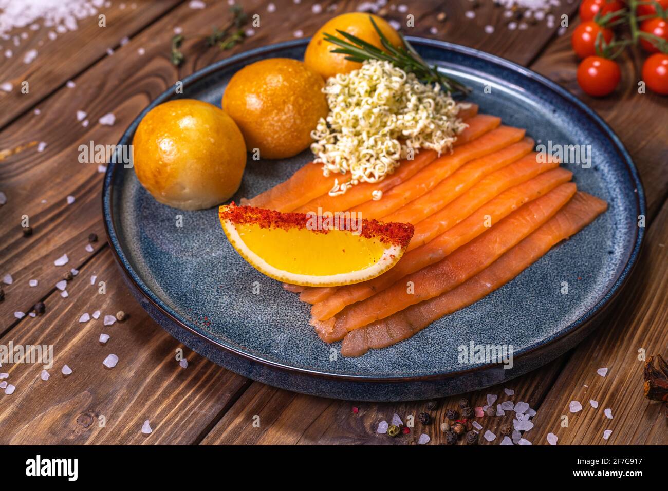 Forellenscheiben auf einem Teller, frische Brötchen, Orange, Chili, Kirschtomaten, Rosmarin auf braunem Holzgrund. Das Konzept des Restaurant-Service. Stockfoto