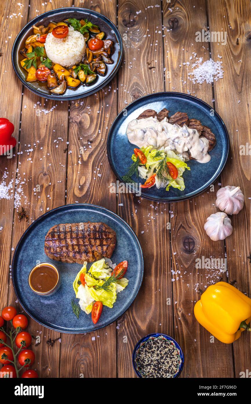 Steak mit Sauce, Salat, Rosmarin, Kirschtomaten auf einem Holzbrett. Flaches Layout. Stockfoto