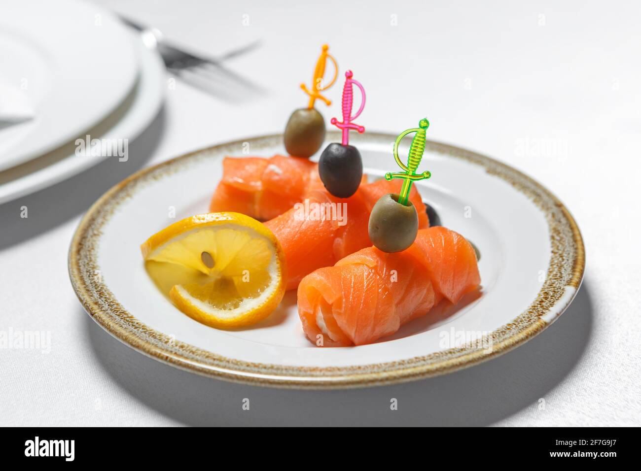 Roter Fisch auf Spieße mit Oliven und Zitrone ist auf einem Teller. Das Konzept der festlichen Tischeinstellung. Stockfoto