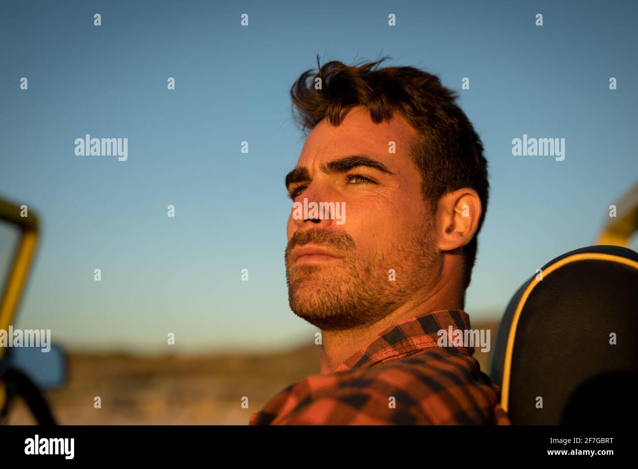 Porträt eines kaukasischen Mannes, der den Sonnenuntergang in einem Baggy am Strand beobachtet Stockfoto