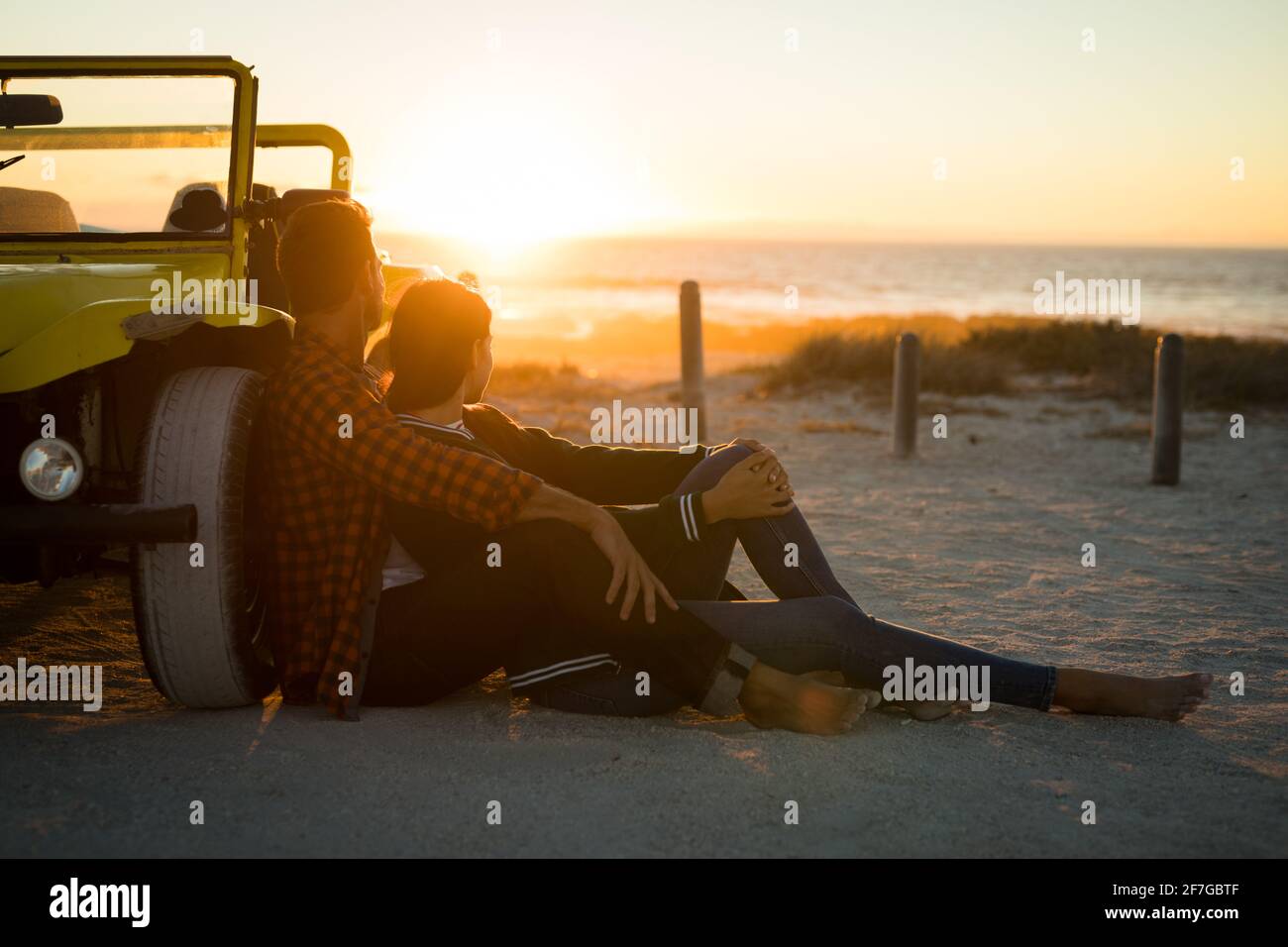 Glückliches kaukasisches Paar, das sich gegen den Strandbuggy am Meer lehnt Sonnenuntergang beobachten Stockfoto