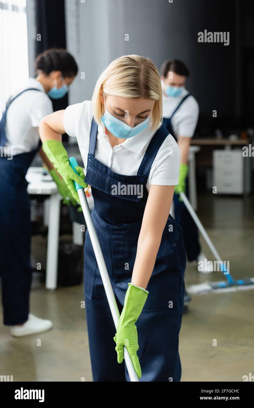 Arbeiter der Reinigungsfirma in der medizinischen Maske hält Mopp in Büro Stockfoto