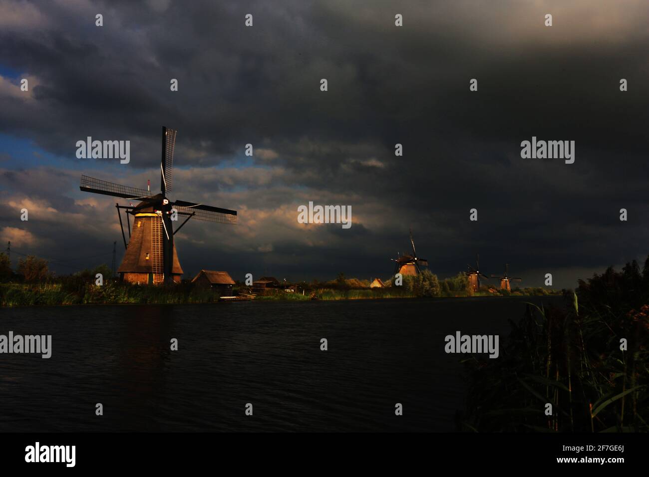 romantische Windmühle am Rande eines Kanals in Kinderdijk mit dramatischer Wolkenstimmung am frühen Abend in Holland, Niederlande Stockfoto