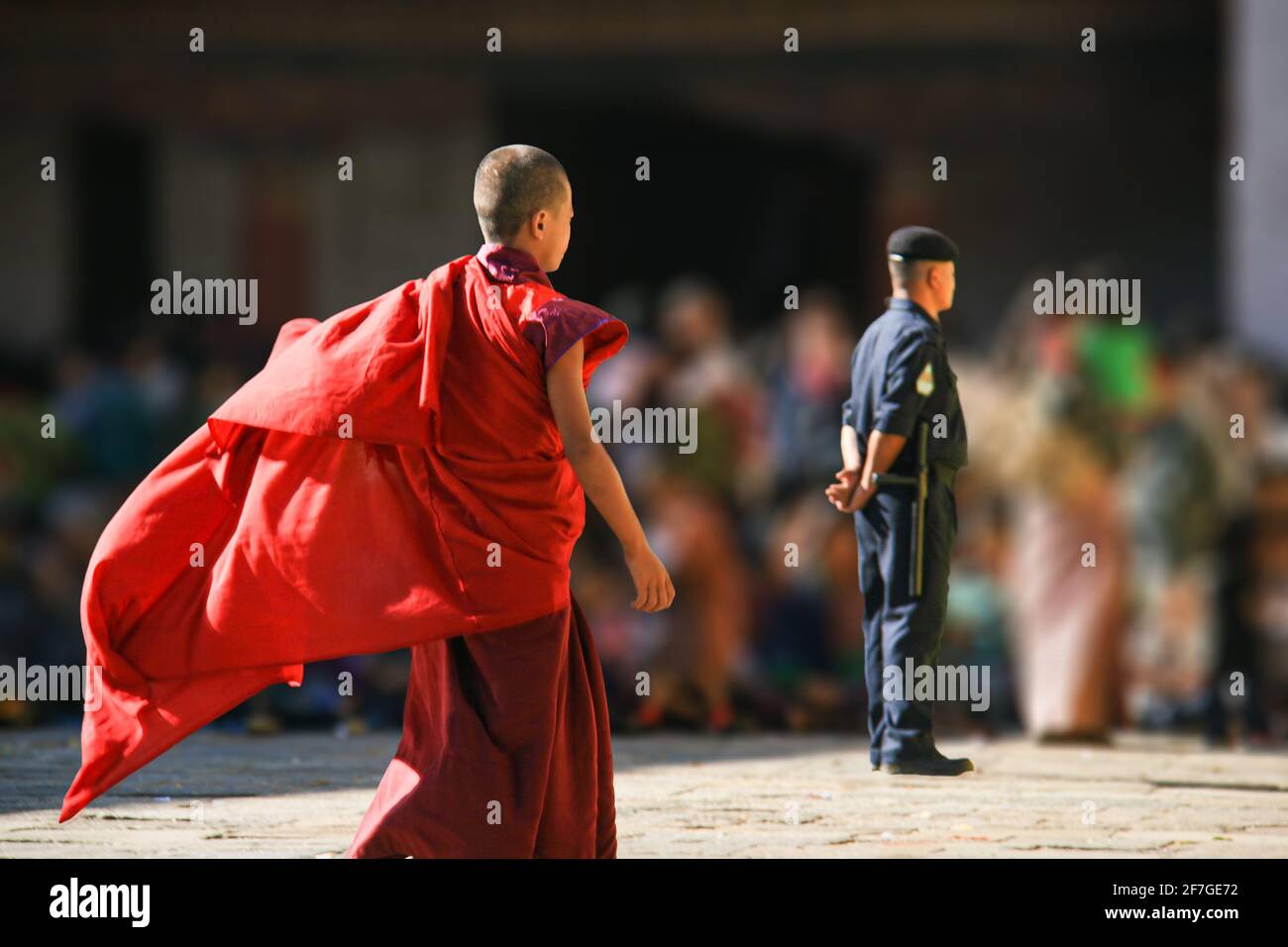 Königreich Bhutan, Asien, Himalaya. Wartende Menschen Menschen drängen sich im Hintergrund. Davor ein Polizist, Sicherheitsbeamter. Ein junger Mönch nähert sich Stockfoto