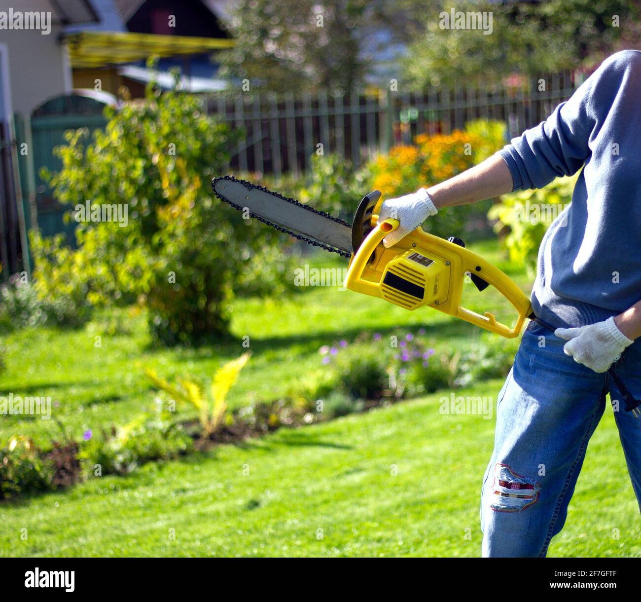 Frauenhände mit gelber Benzinsäge im Freien. Das Konzept der Garten- und Bauarbeit im Garten- und Gemüsegarten. Stockfoto