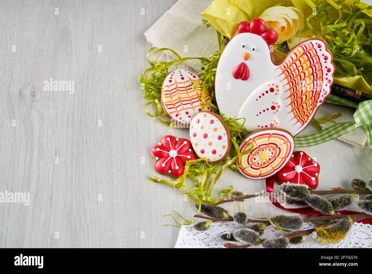 Osterkomposition aus farbigem Lebkuchen, Eiern, Weidenzweigen, Blumen und Spitze auf hellem Holzhintergrund. Konzept des hellen Frühlings und der glücklichen Feiertage Stockfoto