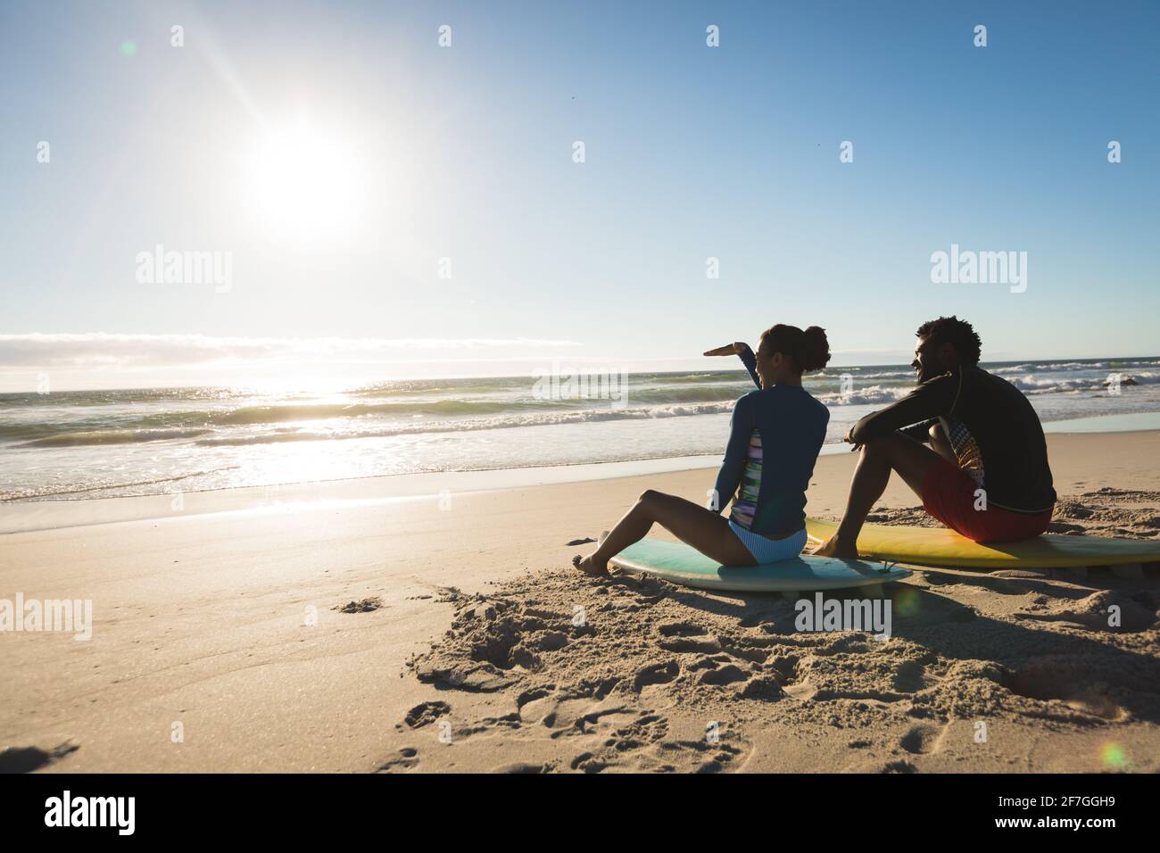 Glückliches afroamerikanisches Paar am Strand, das auf Surfbrettern sitzt Blick auf das Meer Stockfoto