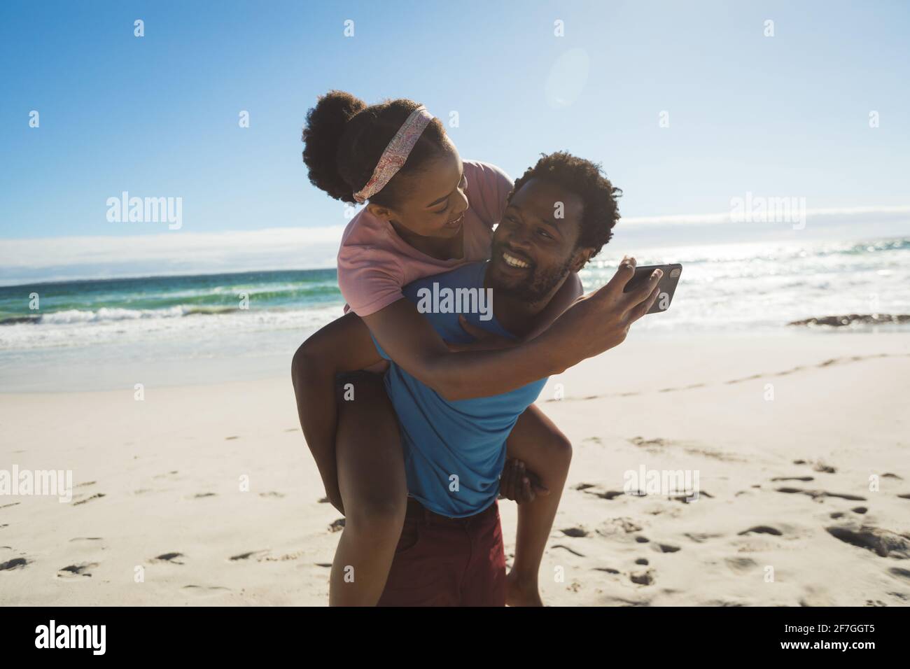 Glückliches afroamerikanisches Paar am Strand am Meer Huckepack Und Selfie machen Stockfoto