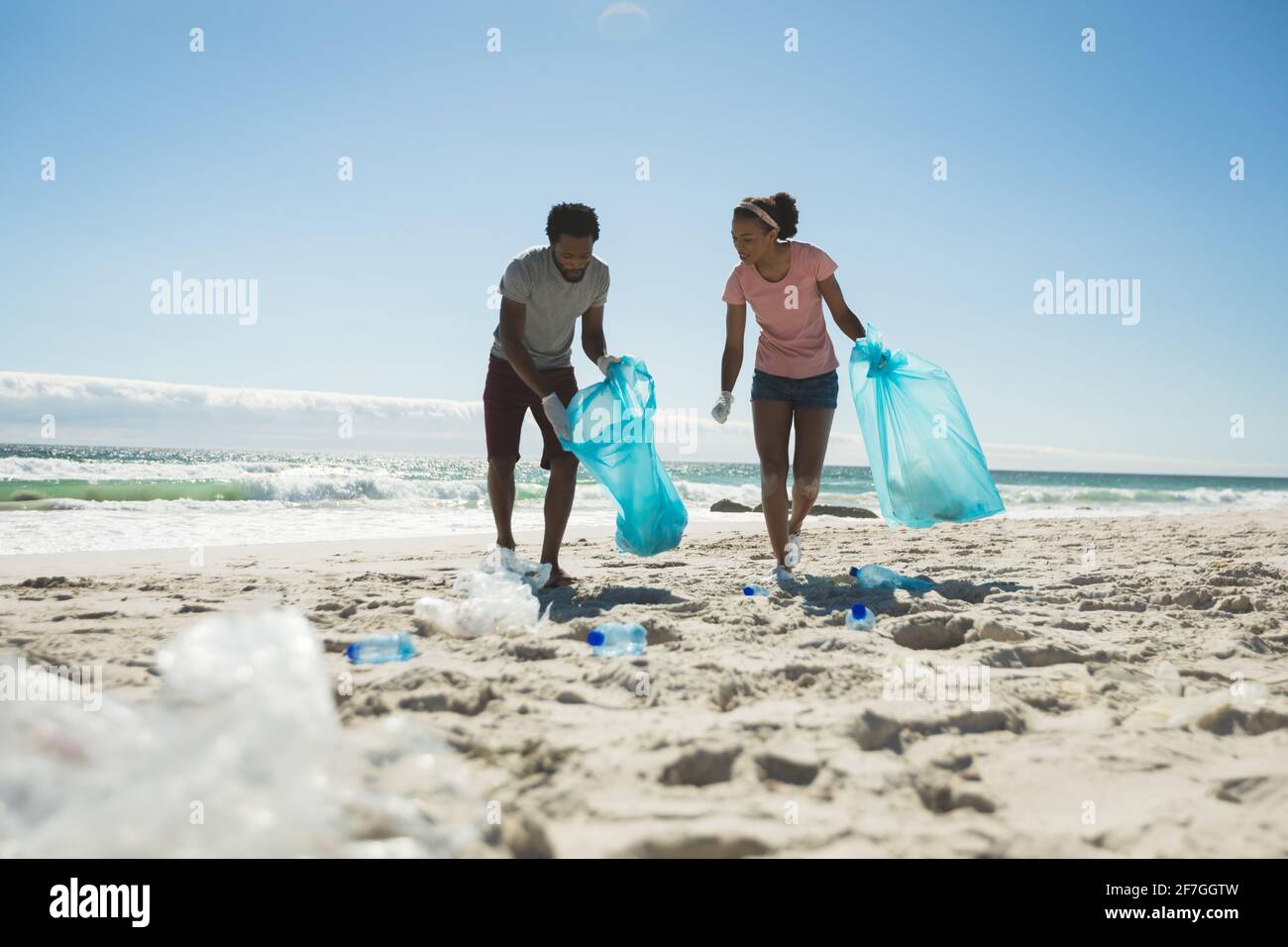 Glückliches afroamerikanisches Paar, das Latexhandschuhe trägt und Müll sammelt Der Strand Stockfoto