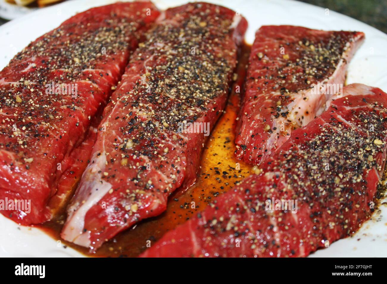 Nahaufnahme von rohen Steaks, gewürzt und auf einem weißen Teller mariniert. Stockfoto